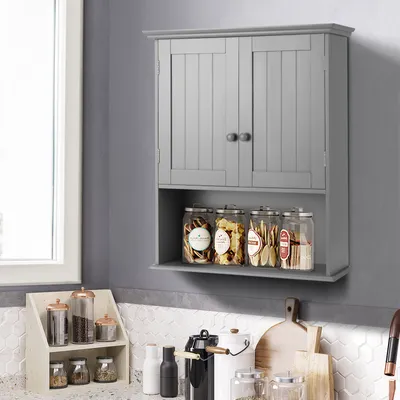 A gray wall-mounted cabinet with two doors and an open shelf below, containing jars of food items. A window is visible on the left, and a countertop with various kitchen items is below the cabinet.