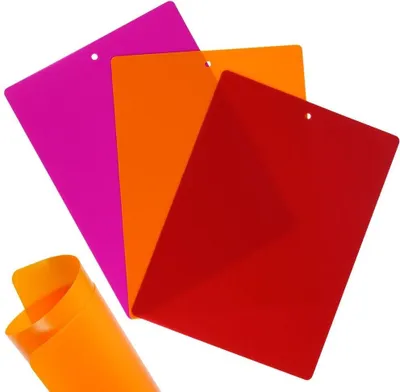 Three flexible cutting mats in pink, orange, and red are fanned out against a white background. A rolled-up orange mat is in the foreground.