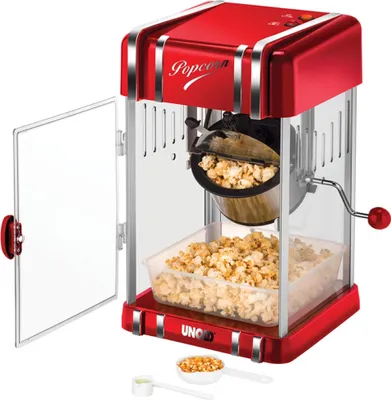 A retro-style red and silver popcorn maker, open with popcorn inside and a small amount of popcorn kernels and a measuring cup in the foreground.