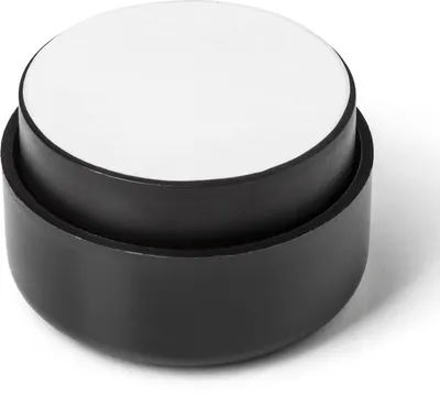 A close-up studio shot of a single black furniture foot with a white top.