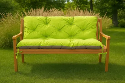 A garden bench with a bright green cushion sits on a grassy lawn, with tall grasses and trees in the background.