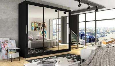 A bedroom with a large black wardrobe with mirrored doors, a bed, and a view of a city from a large window.