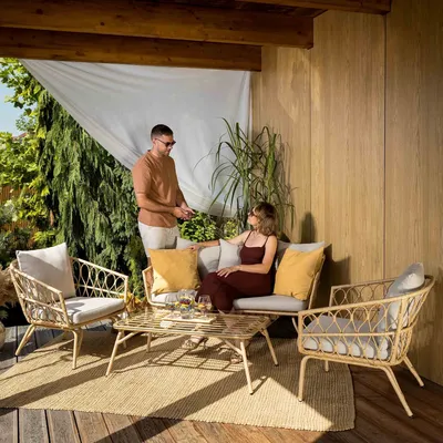A couple is relaxing on a patio set on a wooden deck, surrounded by greenery.