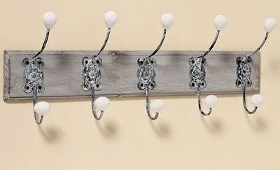 A coat rack with five hooks mounted on a wooden board against a plain wall.