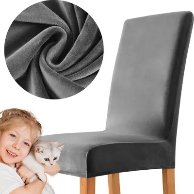A child holding a kitten next to a chair covered with a grey velvet slipcover.