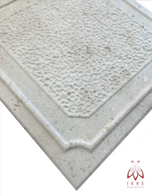 A close-up, angled view of a textured, light-colored panel with a decorative border, presented on a white background.