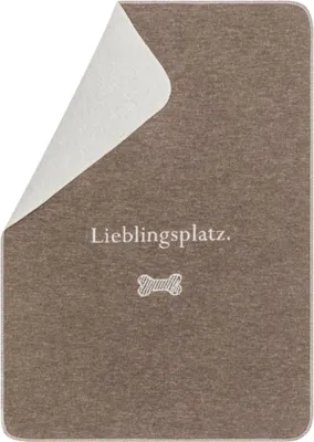 A brown pet blanket with a corner folded back to reveal a white underside. Text and a bone graphic are printed on the blanket.