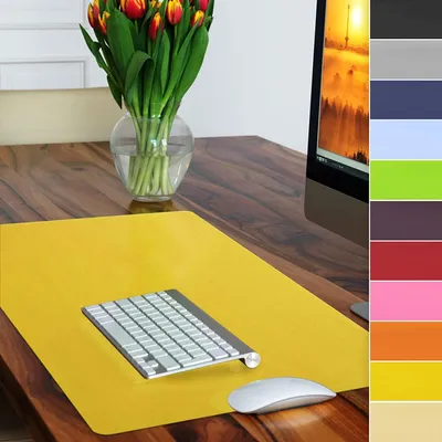 A yellow desk mat with a keyboard and mouse on a wooden table, with a vase of tulips in the background and a color swatch on the right.