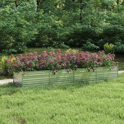 A raised garden bed filled with colorful flowers sits on a grassy lawn, with trees in the background.