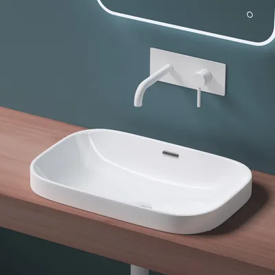 A modern white ceramic sink with a wall-mounted faucet is shown on a wooden countertop against a teal wall.