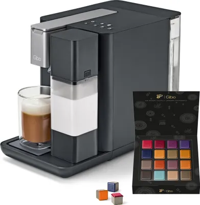 A Tchibo Qbo coffee machine with a glass of coffee and a box of coffee capsules.
