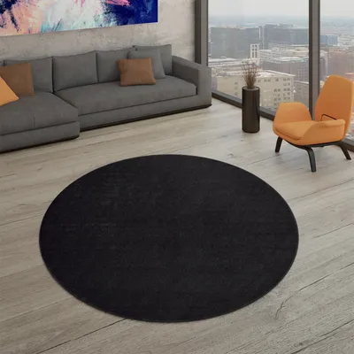 A modern living room with a sectional sofa, an orange accent chair, and a large circular black rug on a light wood floor.