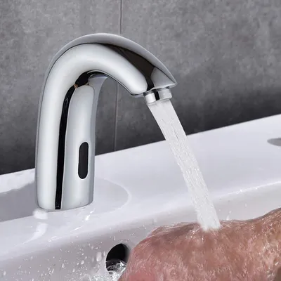 A hand is being washed under a chrome automatic faucet in a bathroom sink.