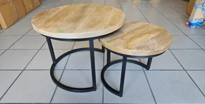 Two round nesting coffee tables with wooden tops and black metal bases are displayed on a tiled floor.