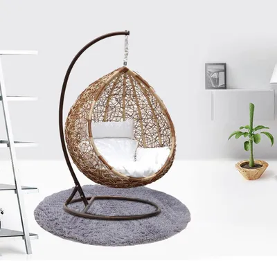 A hanging chair with cushions on a rug, next to a shelf and a plant.