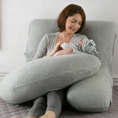 A woman is breastfeeding a baby while using a large U-shaped pregnancy pillow.