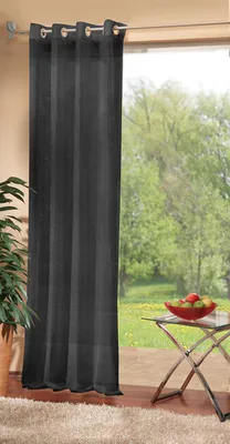 A dark grey curtain hangs in front of a large window with a view of a garden. A small glass table with a bowl of fruit sits to the right of the curtain.