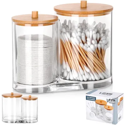 Two clear glass containers with wooden lids, one filled with cotton pads and the other with cotton swabs, are displayed on a clear acrylic base. A smaller set of the same containers is shown in the lower left corner, and a product box is in the lower right