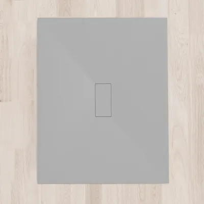 A flat gray shower tray with a rectangular drain opening in the center, placed on a light wood-plank floor.