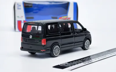 A black toy van is shown from the rear-left angle, with its packaging in the background and a ruler in the foreground.