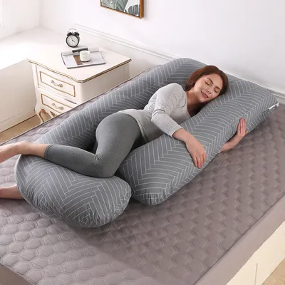 A woman is sleeping on a large U-shaped pregnancy pillow on a bed.