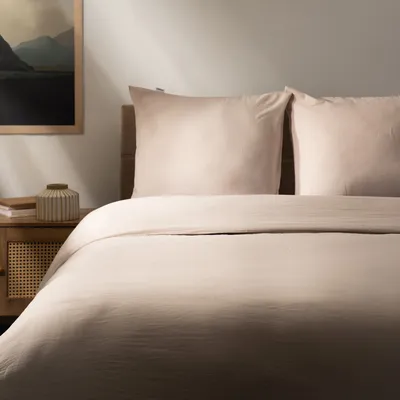 A neatly made bed with beige bedding and pillows.