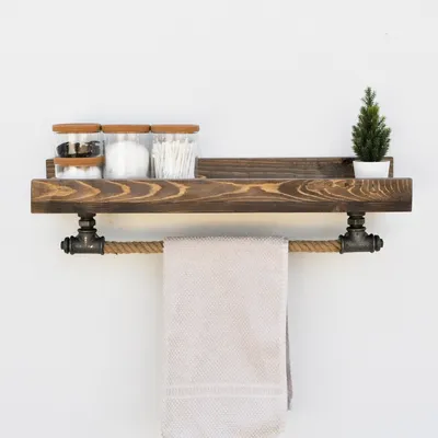 A wooden shelf with industrial pipe accents, holding jars of cotton swabs and a small potted plant, with a towel hanging from the pipe.