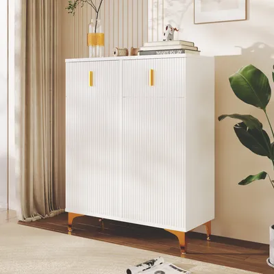 A white cabinet with gold handles and legs, placed in a room with curtains and a plant.