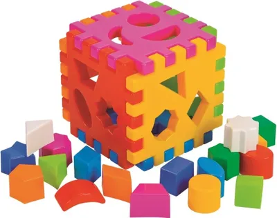 A colorful shape-sorting cube toy with various geometric shapes scattered around it.