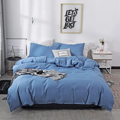 A neatly made bed with blue bedding, a decorative pillow, and a blanket draped over it, set in a bedroom with a framed picture on the wall.