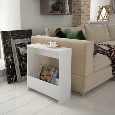A modern white side table with magazines and a cup of coffee next to a sofa in a living room.