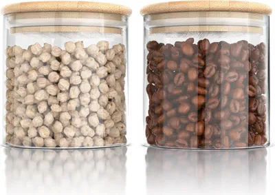 Two glass storage jars with bamboo lids, one filled with chickpeas and the other with coffee beans, displayed on a white reflective surface.