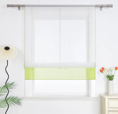 A window with a green and white roman blind, a lamp, and flowers on a table.