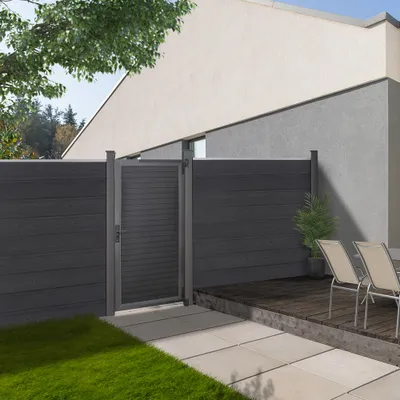 A modern backyard with a dark gray WPC garden gate and fence, a wooden deck with chairs, and a paved walkway.