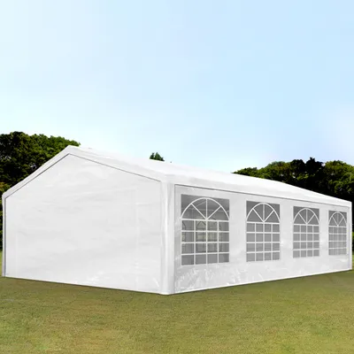 A white party tent with arched windows is set up on a grassy lawn with trees and a blue sky in the background.