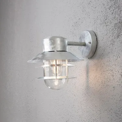A silver wall lamp with a clear glass shade is mounted on a textured gray wall.