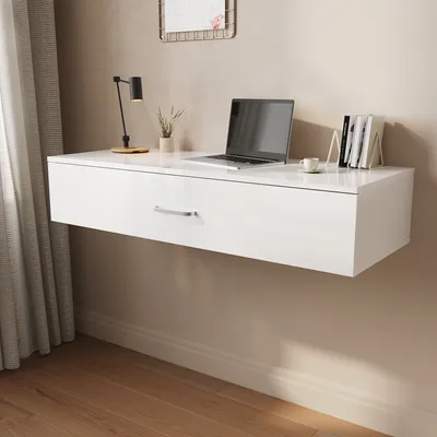 A white floating desk with a laptop, lamp, and books on it, mounted on a wall.