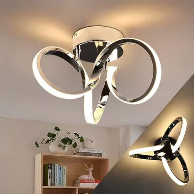 A modern LED ceiling light with a chrome finish, shown in two different perspectives. The main image shows the light fixture mounted on a ceiling, with a shelf unit with decorative items below it. A smaller inset image shows the same light fixture mounted