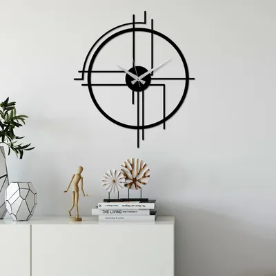 A modern black metal wall clock with a minimalist design is displayed on a white wall above a white cabinet.