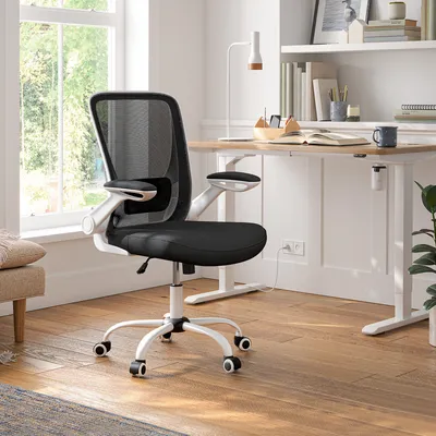 A black mesh office chair with white accents is positioned in a home office setting next to a wooden desk.
