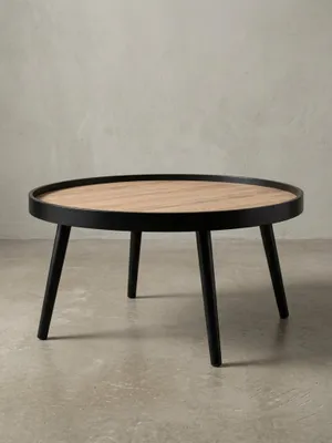 Schräger Blick auf den runden Salontisch, der die erhöhte Kante der Tischplatte und die elegant gespreizten schwarzen Holzbeine zeigt._#sku_BARWL6.496#