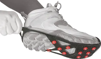 A person is putting on ice cleats over a hiking boot.