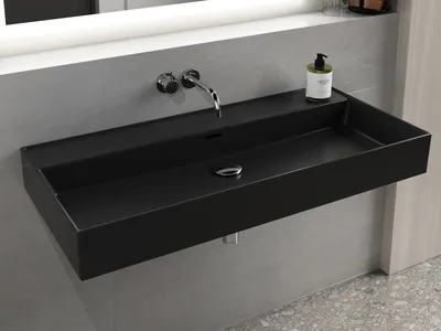 A modern black matte washbasin mounted on a gray tiled wall, with a chrome faucet and a soap dispenser on the shelf.