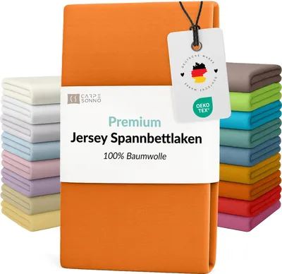 A stack of folded bedsheets in various colors, with an orange sheet prominently displayed in the foreground.