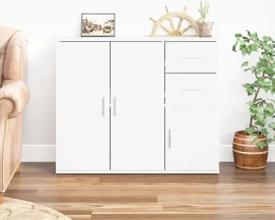 A white sideboard with doors and drawers, decorated with items on top, stands in a room with a couch and a plant.