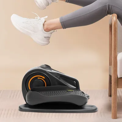 A person's legs and feet are shown exercising on a compact elliptical machine placed on the floor.
