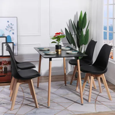 A dining set with black chairs and a black table with wooden legs, set in a room with artwork and a large plant.
