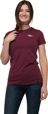 Dame trägt ein burgunderfarbenes T-Shirt von Black Diamond; lächelt und steht mit einer Hand im Haar.