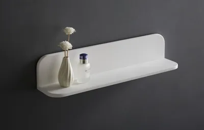 A white shelf mounted on a dark gray wall, with a small vase of flowers and a bottle on it.