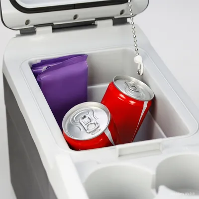 A close-up shot of the interior of a portable cooler, showing two soda cans and a purple package.